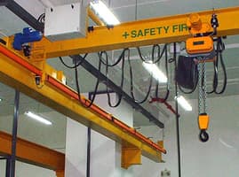 Yellow overhead crane with an electric chain hoist inside a workshop