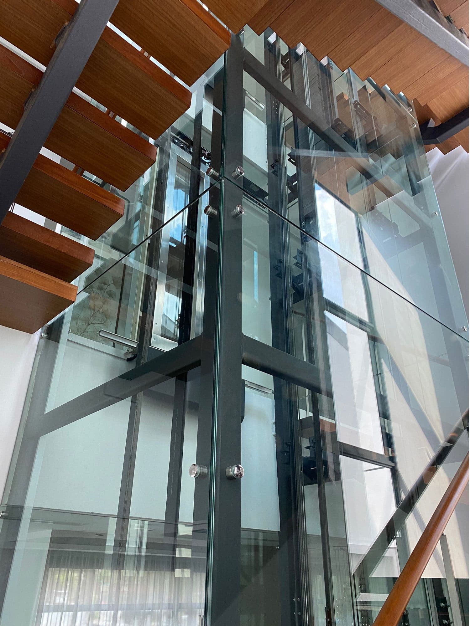 Glass-enclosed lift shaft beside a timber staircase