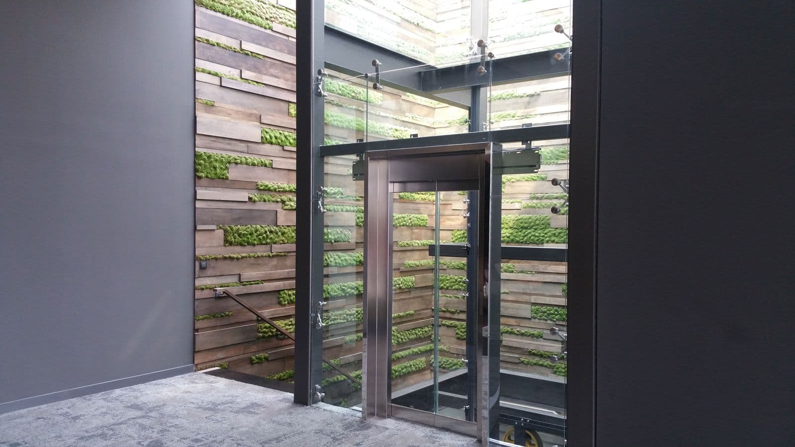 Stainless steel lift door beside a moss and timber feature wall